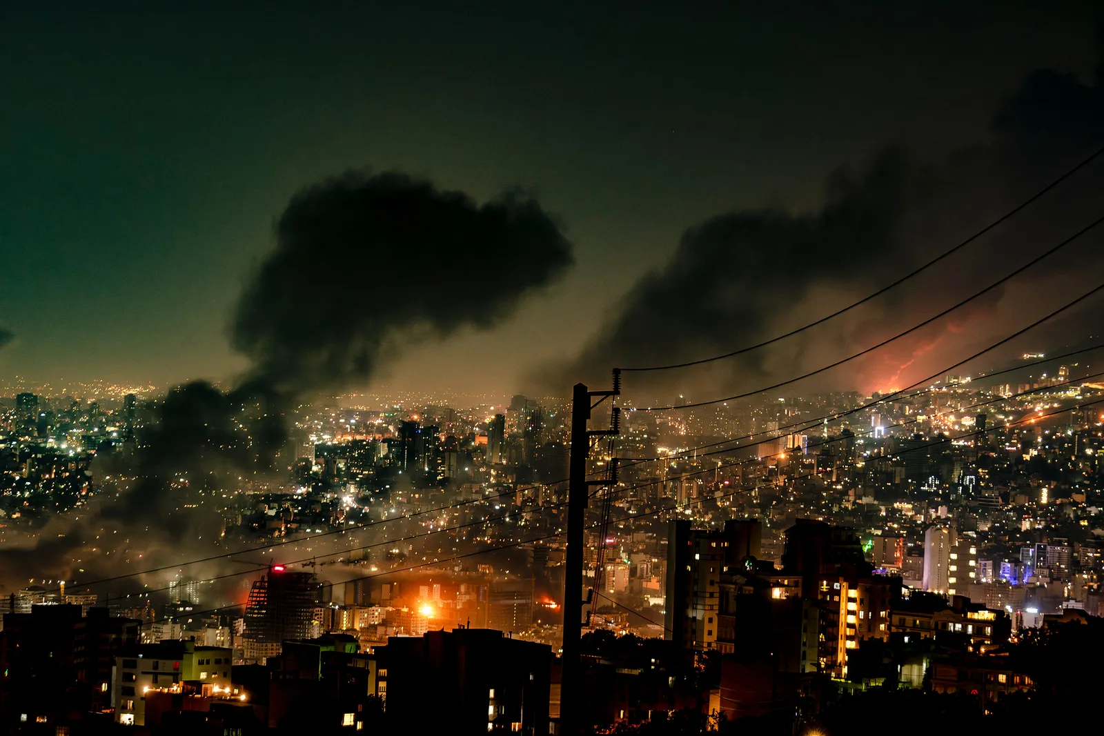 Orașul afectat de atacuri aeriene, cu fum și lumini în noapte.