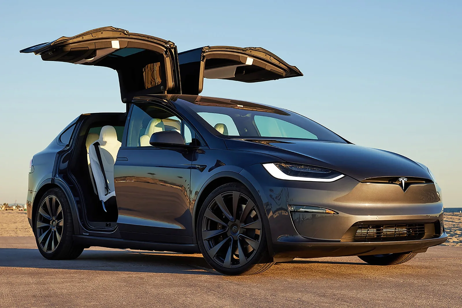 Tesla Model X cu uși de tip aripă de pescăruș, pe plajă la apus.