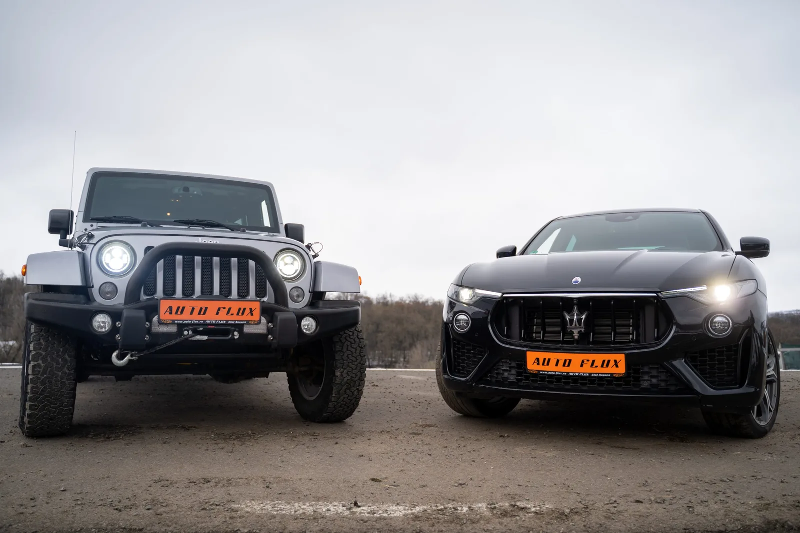 Două mașini de lux parcate pe un teren deschis, una off-road și alta sport.