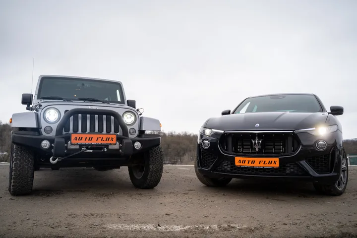 Două mașini de lux parcate pe un teren deschis, una off-road și alta sport.