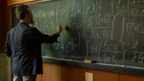 Profesor scriind formule pe tablă într-o sală de clasă universitară.