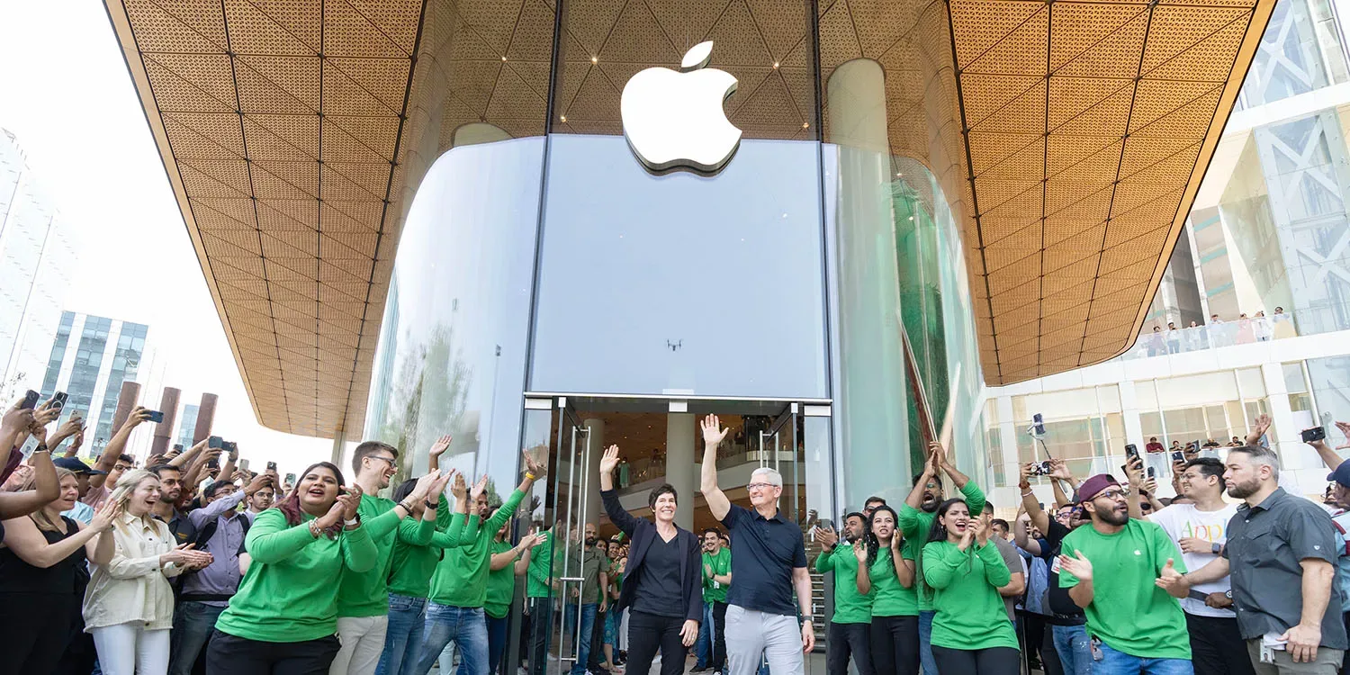 Oameni entuziasmați la deschiderea unui magazin Apple, cu logo-ul companiei în fundal.