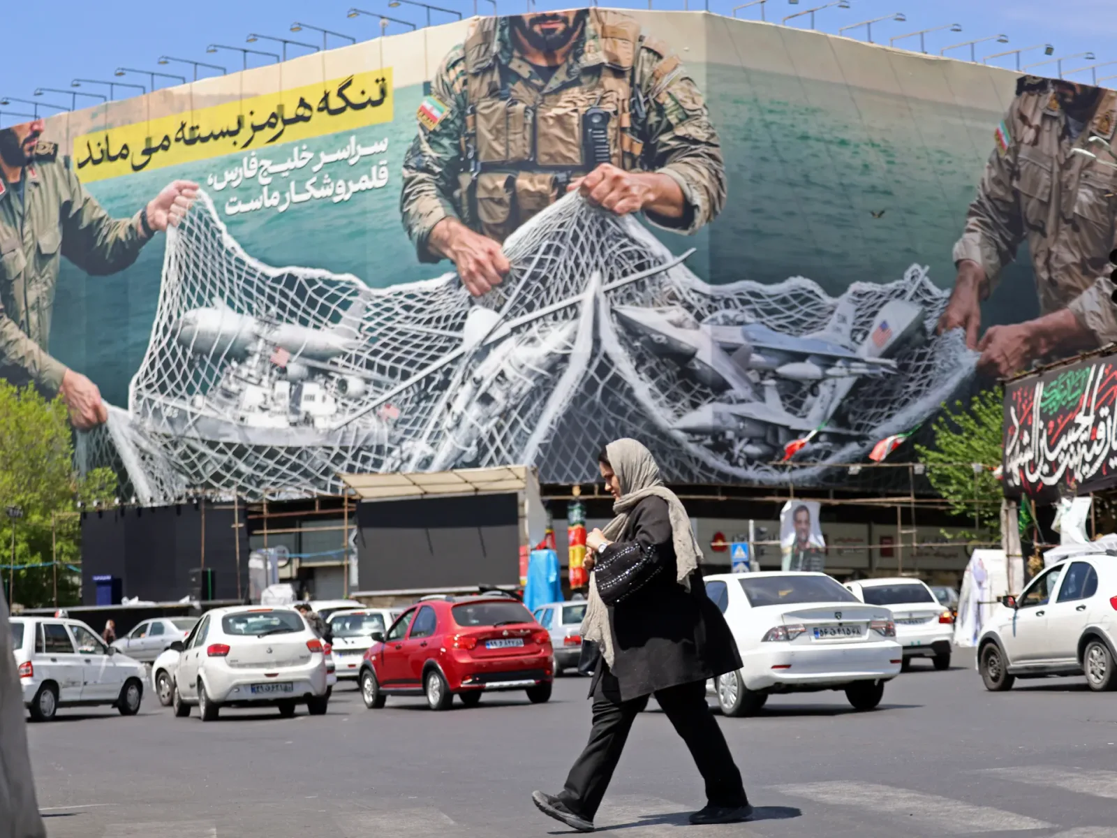 O femeie trece pe lângă un mural cu soldați în Teheran.