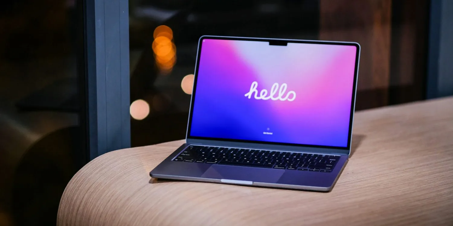 Laptop deschis pe o masă, cu un ecran colorat care afișează cuvântul 'hello'.