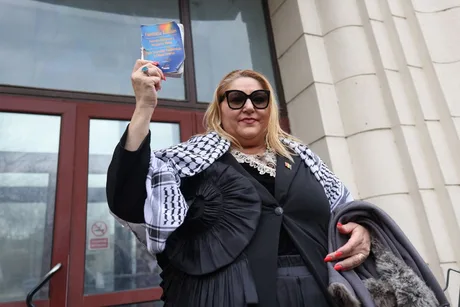 Diana Șoșoacă ține un obiect în mână, în fața unei clădiri oficiale.