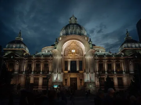 Clădirea CEC Bank iluminată pe timp de noapte, evidențiind arhitectura sa impresionantă.