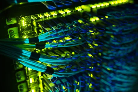 Cabluri de rețea conectate la un server, iluminat în verde și albastru.