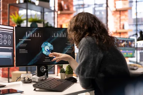 Angajat analizând date pe un monitor, folosind tehnologie avansată.