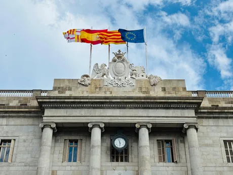 Clădire istorică din Spania cu steaguri naționale și europene.