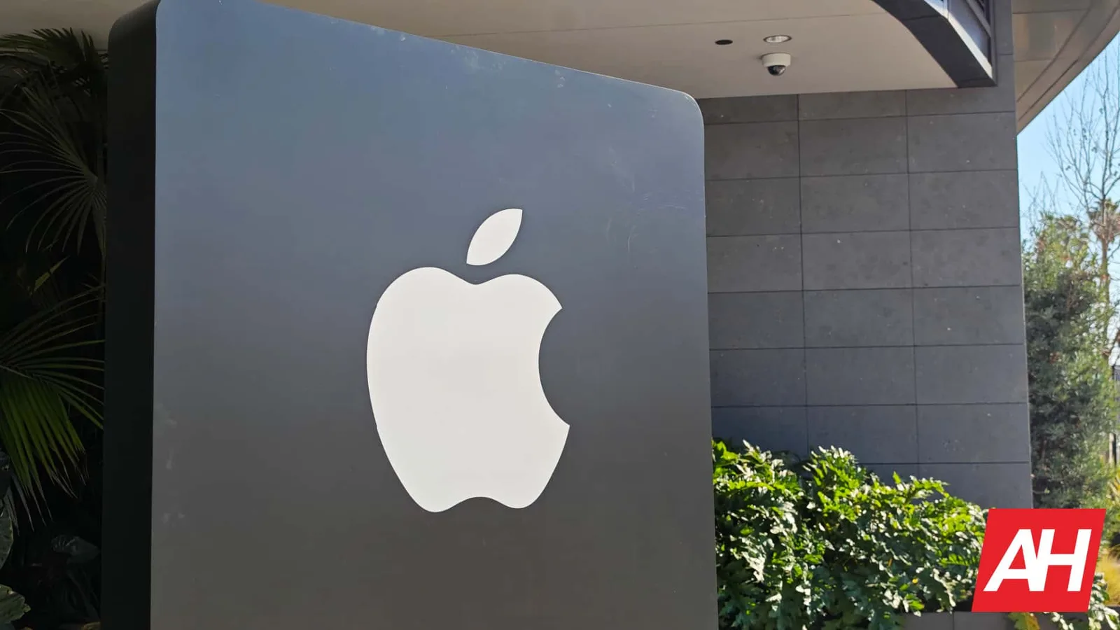 Logo-ul Apple pe fundalul unei clădiri moderne, înconjurat de verdeață.