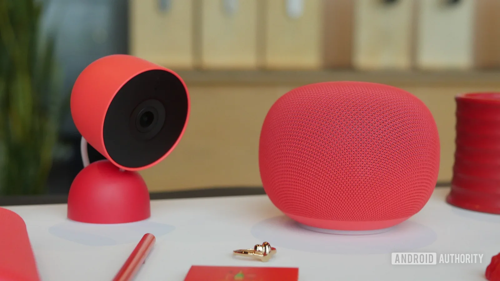 Dispozitive Google Home și Nest Cam în nuanțe roșii, pe o masă.