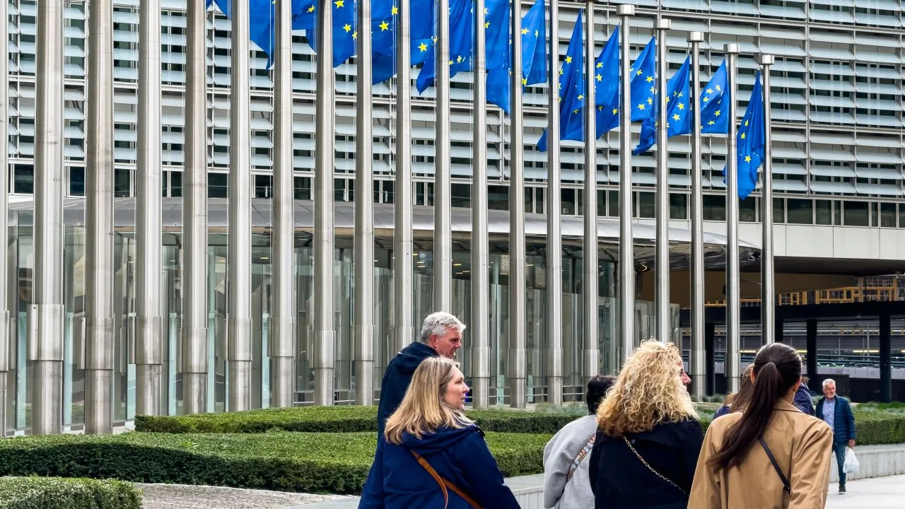 Grup de persoane în fața clădirii Comisiei Europene, cu steaguri ale UE în fundal.