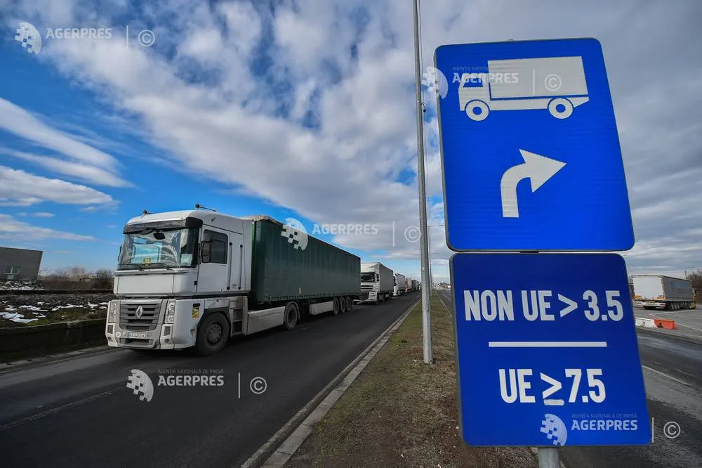 Camioane în trafic pe un drum european, semne de direcție vizibile.