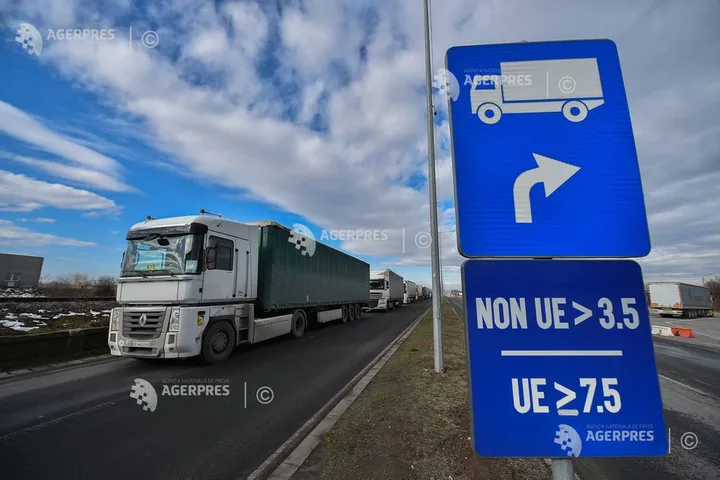 Camioane în trafic pe un drum european, semne de direcție vizibile.