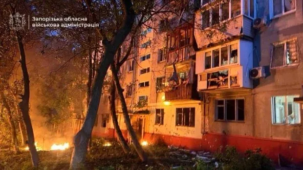 Clădire avariată în urma unui atac, cu foc în jur și feronerie distrusă.