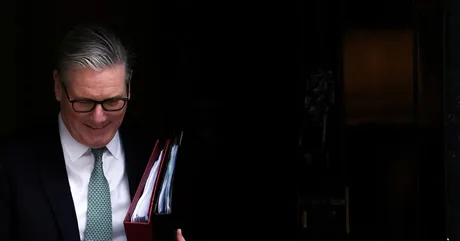 Keir Starmer părăsește clădirea cu documente în mână, zâmbind.