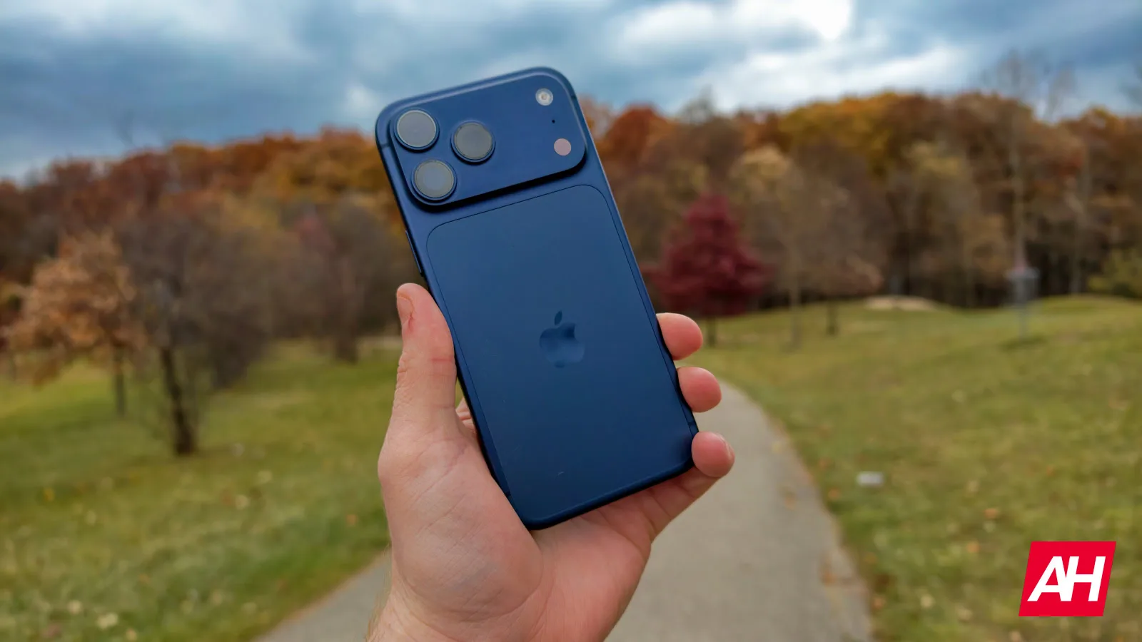 Un utilizator ține un iPhone pe un fundal de toamnă.