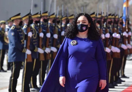Ceremonie oficială cu soldați în uniformă și o femeie în mantie albastră.