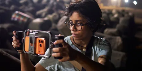 Cineast filmând cu iPhone 17 Pro Max pe un fundal stâncos, în condiții de lumină slabă.