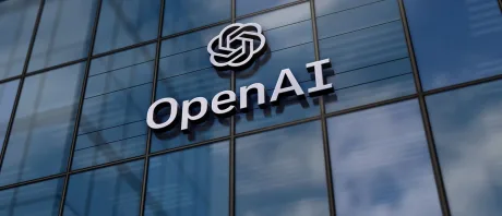 Logo-ul OpenAI pe o clădire modernă, reflectând cerul.