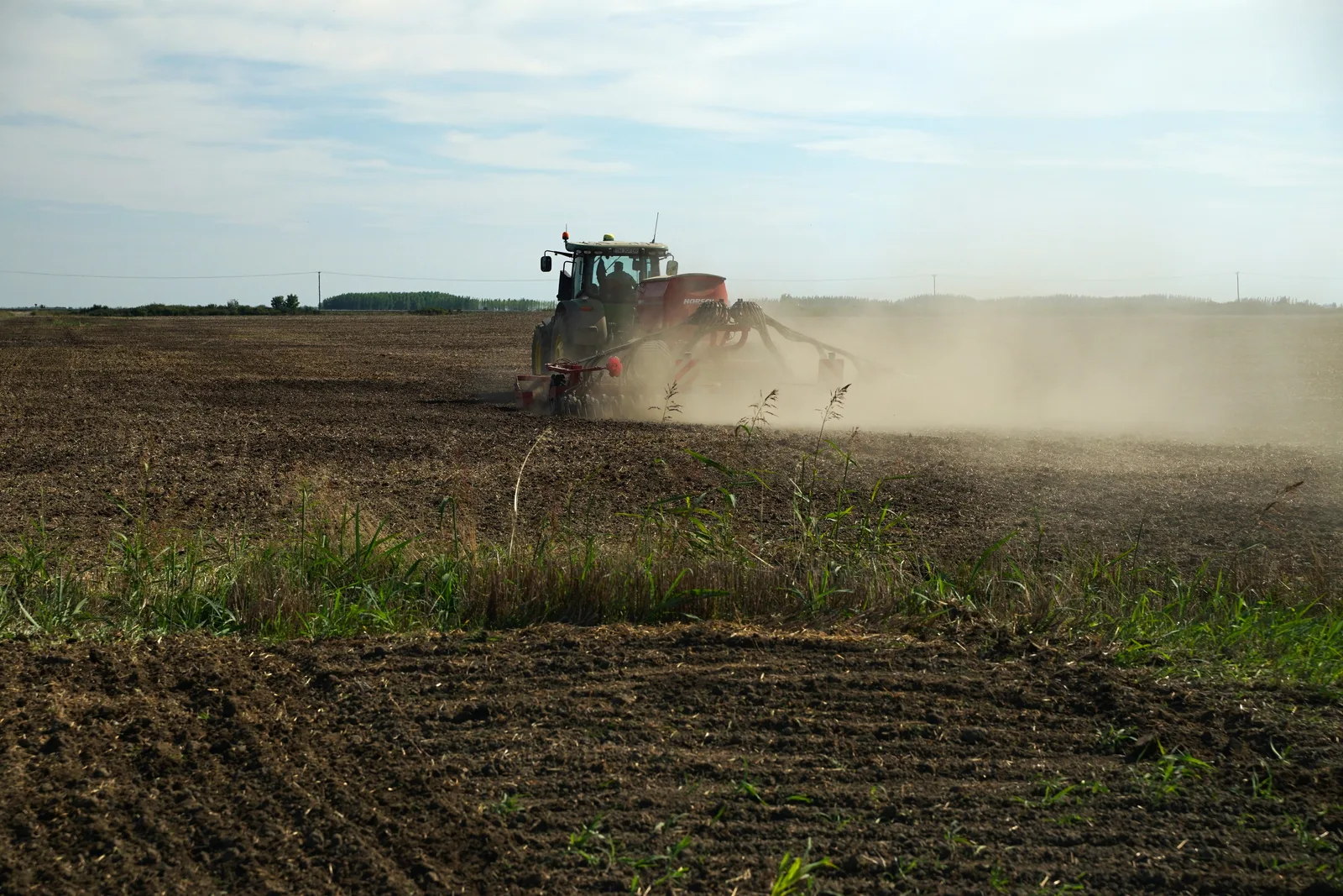 Fermier lucrând un teren agricol cu un tractor în timpul zilei.