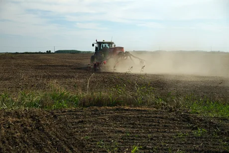 Fermier lucrând un teren agricol cu un tractor în timpul zilei.