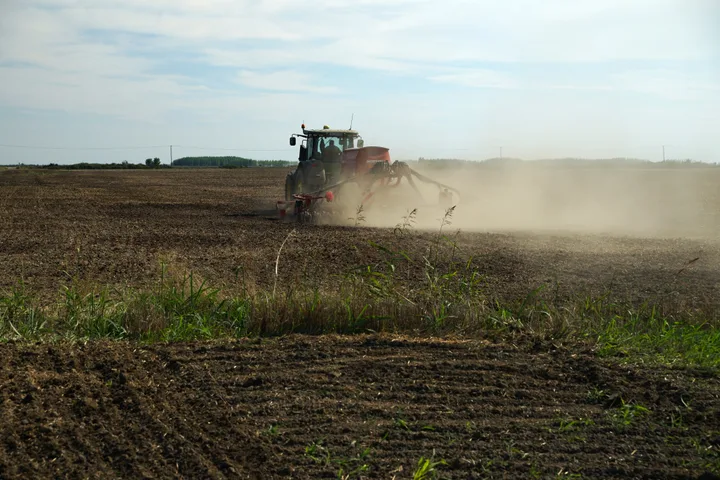 Fermier lucrând un teren agricol cu un tractor în timpul zilei.