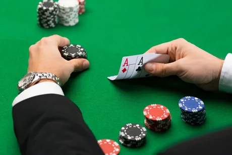Oameni jucând cărți pe o masă de poker, cu fise colorate în jur.