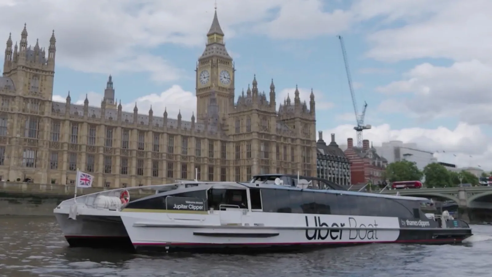 Ambarcațiune Uber Boat navigând pe apă, cu clădiri istorice în fundal.