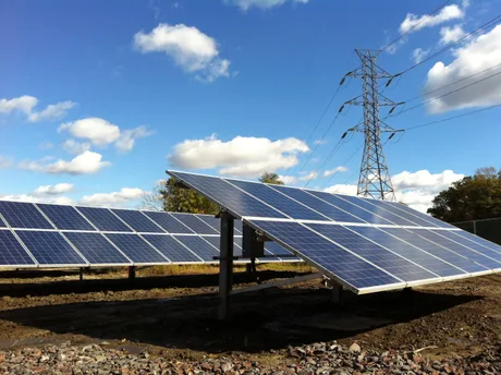 Panouri solare instalate pe un teren, sub un cer senin cu nori.