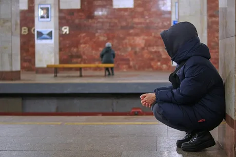 Un tânăr așezat pe podea într-o stație de metrou, reflectând la viață.