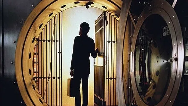 Un bărbat stând în fața unei uși de seif deschise, contemplând interiorul.