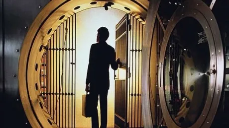 Un bărbat stând în fața unei uși de seif deschise, contemplând interiorul.