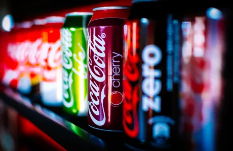 Diferite tipuri de băuturi răcoritoare pe raft, cu etichete colorate.