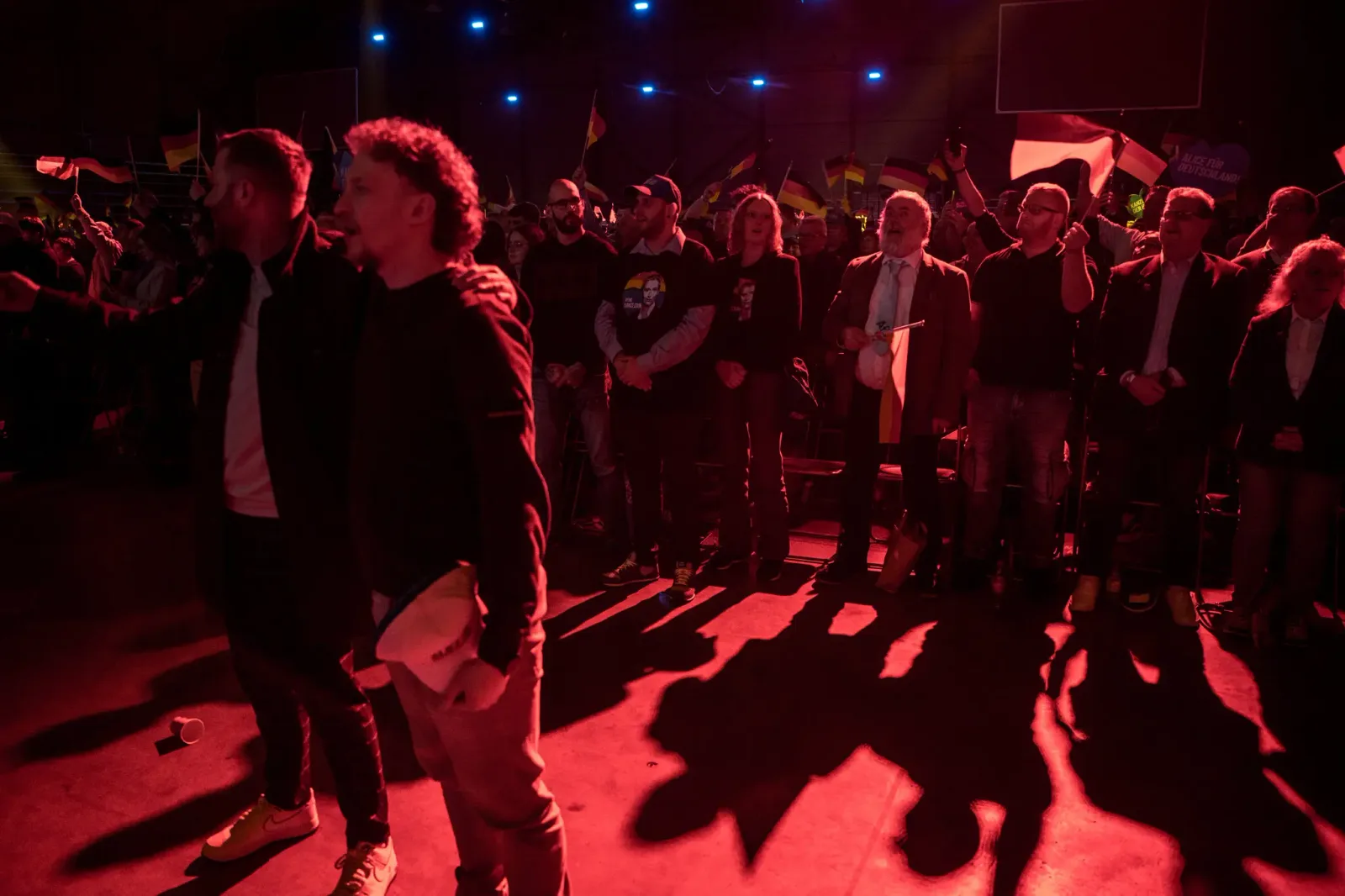 Oameni adunați la un miting politic, cu steaguri și lumini strălucitoare.