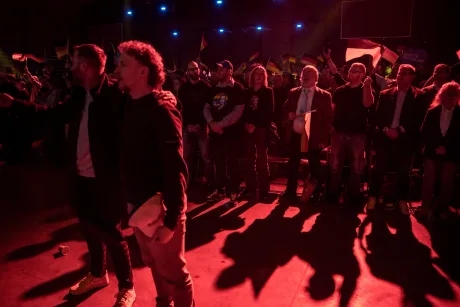 Oameni adunați la un miting politic, cu steaguri și lumini strălucitoare.