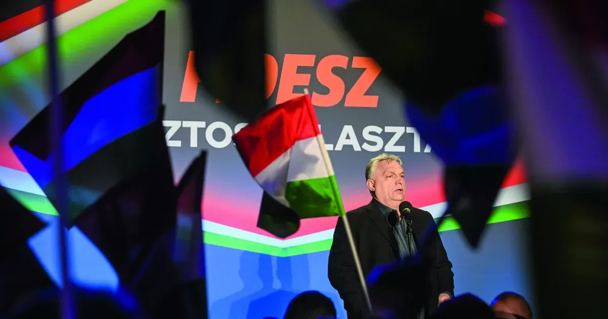 Viktor Orbán vorbește la un miting electoral în Ungaria, înconjurat de steaguri.