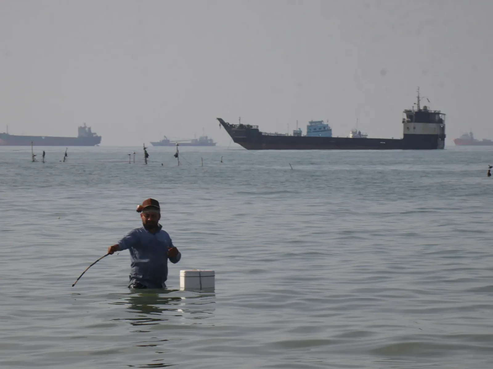 Un bărbat în apă, în fundal un petrolier navigând pe mare.