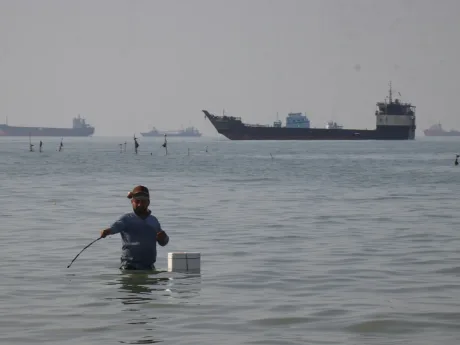 Un bărbat în apă, în fundal un petrolier navigând pe mare.