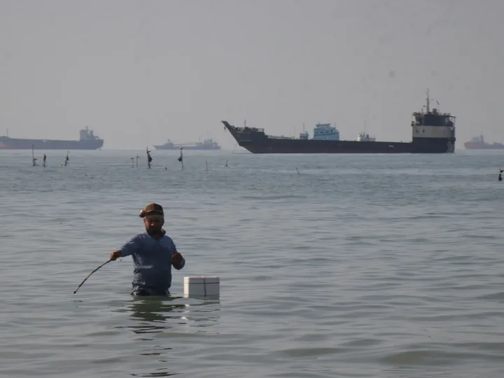 Un bărbat în apă, în fundal un petrolier navigând pe mare.