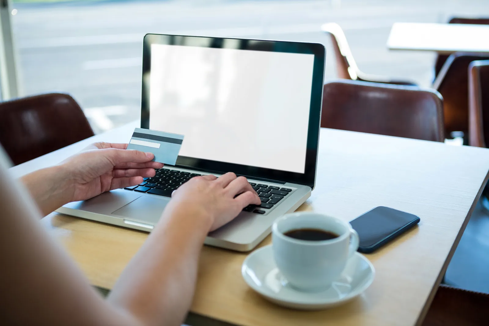 Persoană lucrând la laptop, cu o cană de cafea și un card de credit.