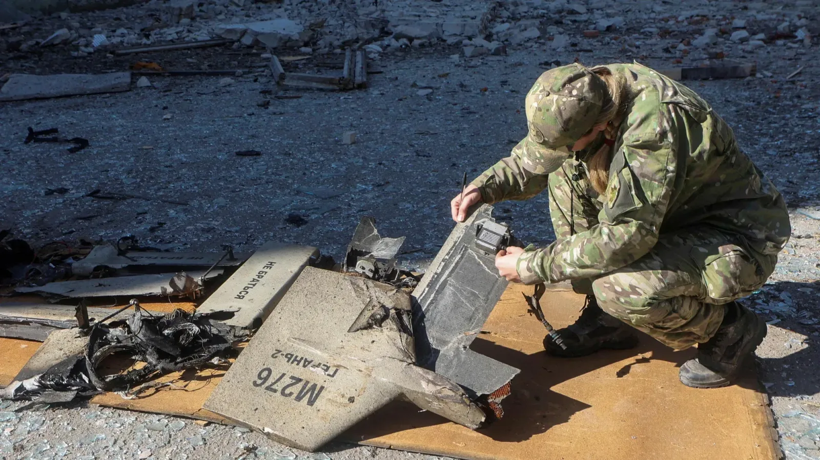 Soldat inspectând resturi de dronă distrusă pe teren.