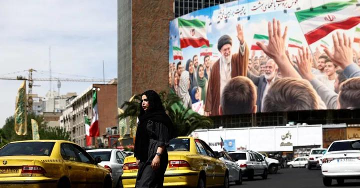 O femeie în hijab trece pe lângă un mural cu lideri iranieni în Teheran.