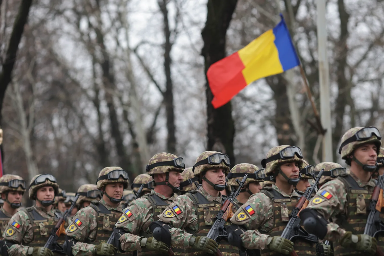 Soldați români în uniformă, defilând cu steagul național.