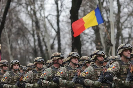 Soldați români în uniformă, defilând cu steagul național.