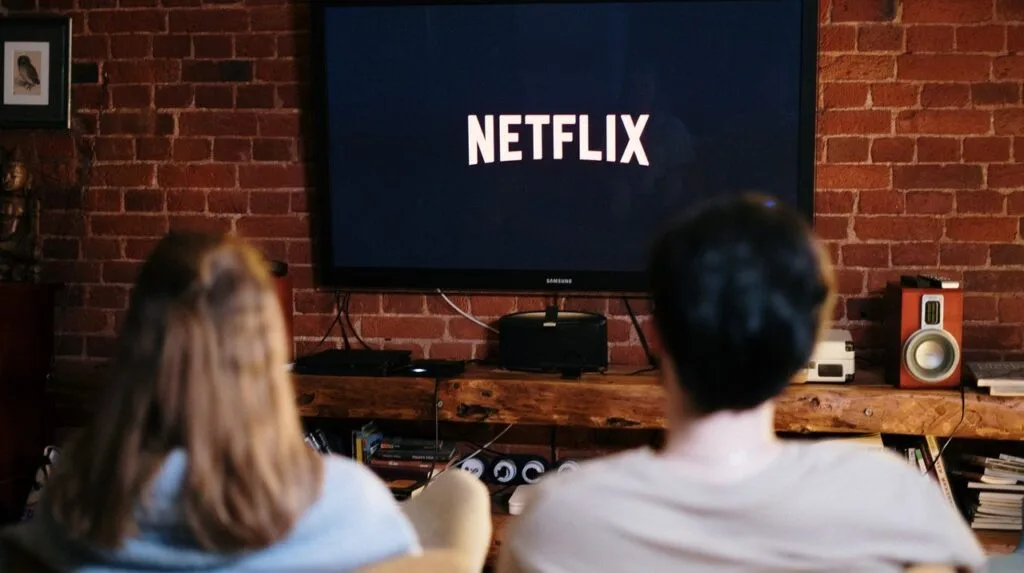 Două persoane urmăresc un film pe Netflix într-un living confortabil.