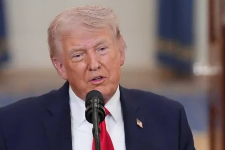 Donald Trump vorbește la un microfon, în fundal drapelul american.