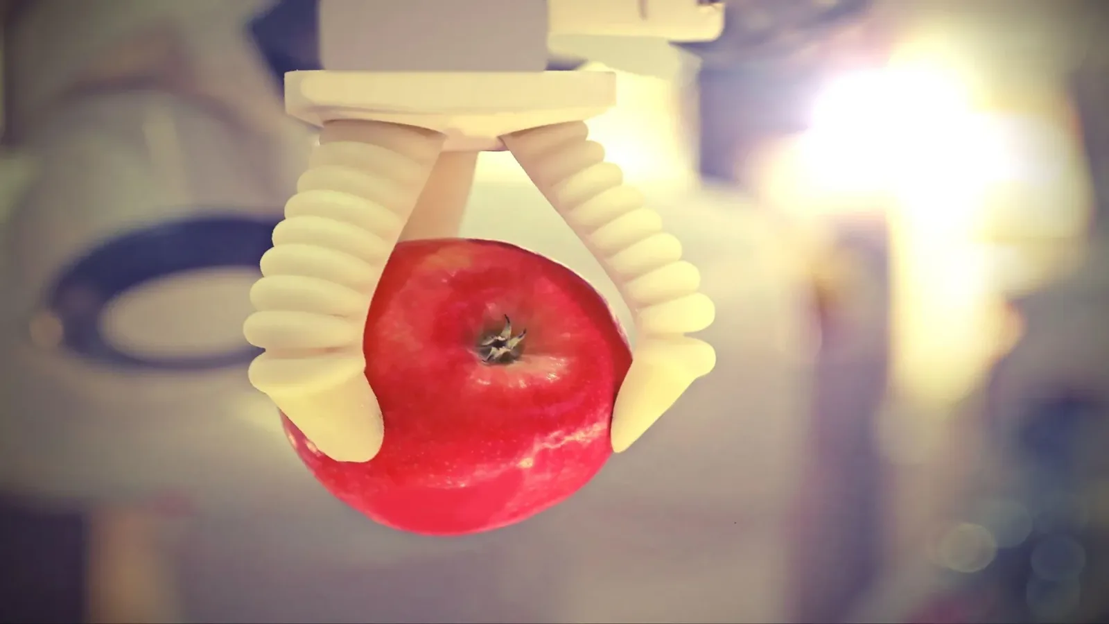 Clește robotic care prinde un măr roșu, demonstrând tehnologia mușchilor artificiali.