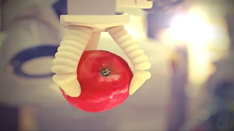 Clește robotic care prinde un măr roșu, demonstrând tehnologia mușchilor artificiali.