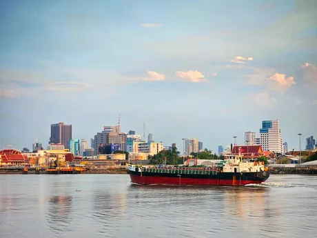 Nava comercială navigând pe un râu, cu orașul în fundal.